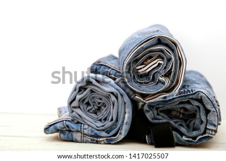 Roll blue denim jeans arranged in stack. Lot of different jeans on white wooden table. 