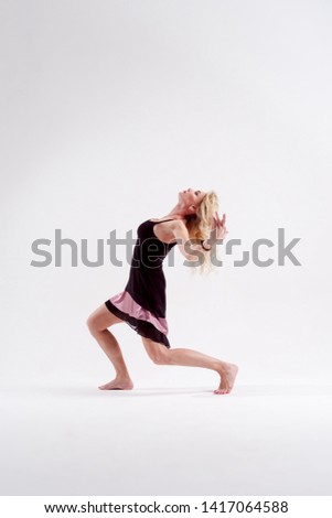 Photo of dancing blonde looking down with raised arms in studio