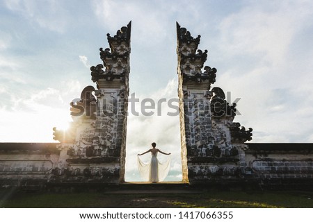 Welcome to Bali. Travel concept. Woman enjoying sunset on Balinese famous symbol - traditional gate in temple with beautiful view. Royalty-Free Stock Photo #1417066355