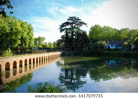 View of a Small Pond With a Small Arched Brick Bridge Spanning Across the Bridge With its Reflection in the Pond on A Bright Blue Sunny Evening During The Summer