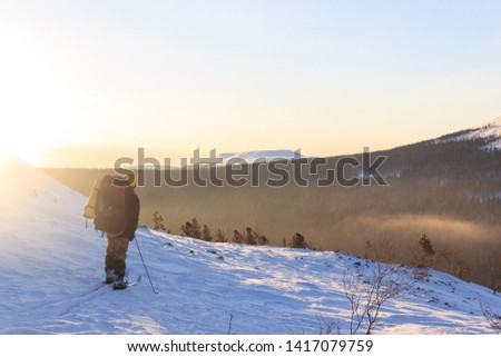 A tourist skier stands on a snowy slope and looks into the distance. Illuminated photo