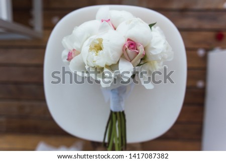 Overhead view of beautiful and stylish pastel wedding bouquet with roses and peonies lying on a white chair. Wedding details and decorations.