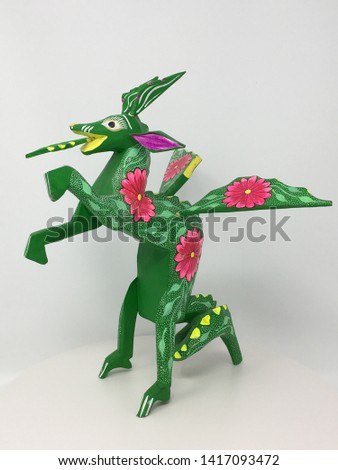 Mexican Alebrije folk art are wooden figures that are crafted by hand and hand painted in the state of Oaxaca in Southern Mexico. This example is a colorful green dragon with pink floral designs.