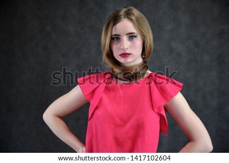 Photo portrait of a beautiful girl of the woman on a dark gray background with long beautiful hair in a red sleeveless jacket standing right in front of the camera and smiling. Made in a studio.