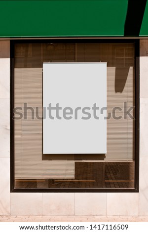Rectangular blank billboard on glass window with blinds
