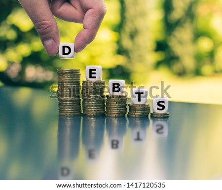 Symbol for decreasing debts. Dice form the word "depts" which are placed on declining high stacks of coins. Royalty-Free Stock Photo #1417120535