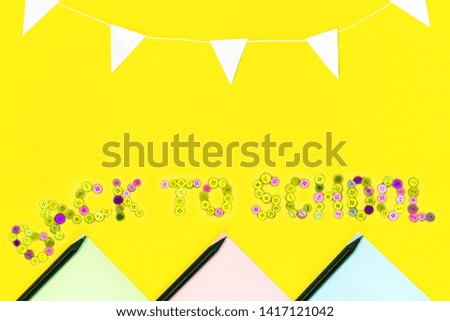 Text from color buttons back to school on yellow background with colored paper, black pencils, garland of white flags.