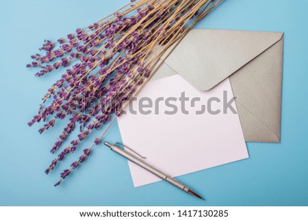 Lavender flowers and blank paper with an envelope on a blue background. View from above. mock up