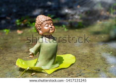 selective focus on chinese ceramic young monk doll standing on green leaf.Blurred nature background. 