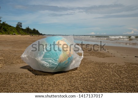 Globe inside a plastic bag by the beach symbolising the world's plastic problem 