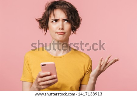 Image of a confused young beautiful woman posing isolated over pink wall background using mobile phone. Royalty-Free Stock Photo #1417138913