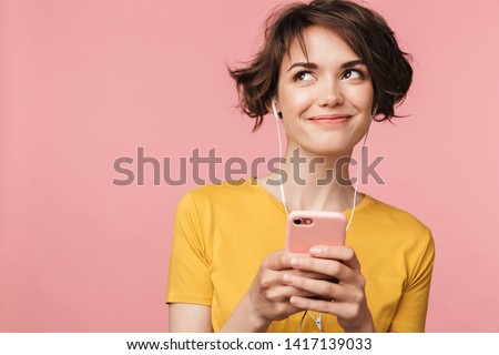 Image of a happy young beautiful woman posing isolated over pink wall background listening music with earphones using mobile phone. Royalty-Free Stock Photo #1417139033