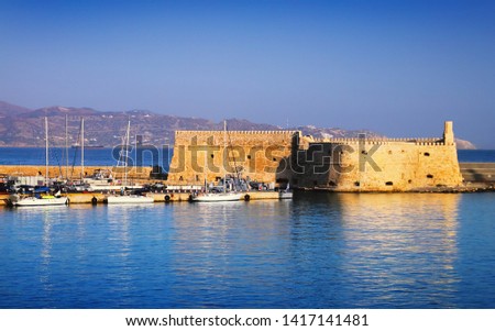 Beautiful cityscape - old venetian port, ancient Koules fort, yachts on the background of bright blue sea water and sky at evening, harbour of Heraclion, island of Crete, Greece, Southern Europe