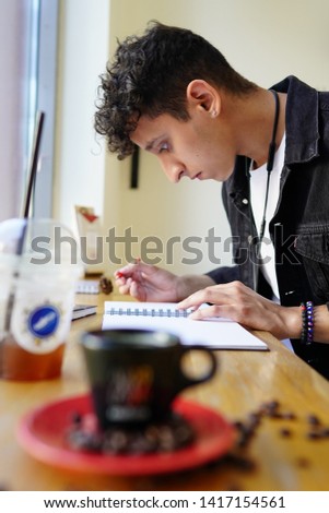A young guy sits in a coffee shop and draws a picture
