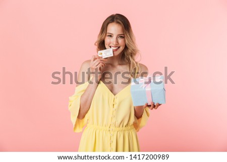 Image of a beautiful excited emotional happy young blonde woman posing isolated over pink wall background holding present gift box and credit card.