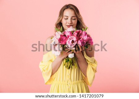 Image of a beautiful amazing young blonde woman posing isolated over pink wall background holding flowers.