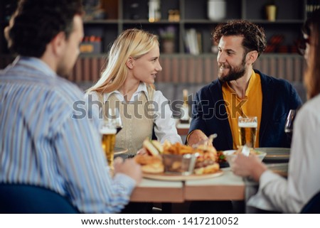 Multiethnic friends sitting at restaurant, drinking alcohol, chatting and having burgers for dinner.