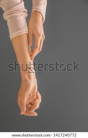 Woman with painted AQUARIUS Zodiac sign on her wrist against grey background