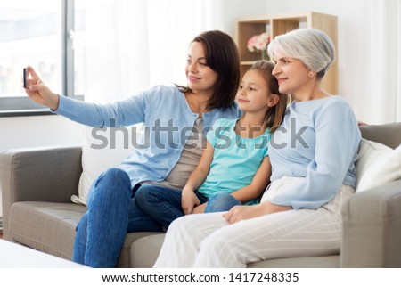 family, generation and technology concept - happy mother, daughter and grandmother taking selfie by smartphone at home