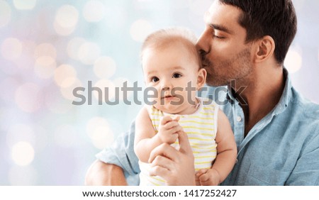 family, parenthood and people concept - happy father kissing little baby daughter over lights background