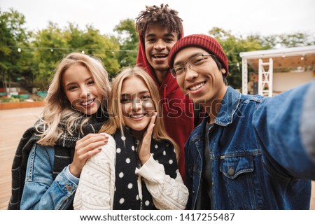 Group if cheerful multiethnic friends teenagers spending fun time together outdoors, taking selfie