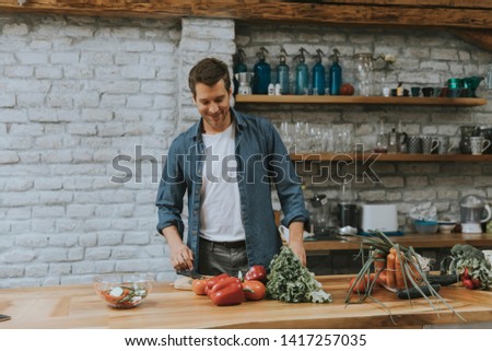 Young man chopping fresh vegetables in the rustic kitchen and preparing healthy meal