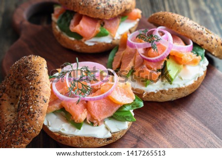 Lox - Everything bagel with smoked salmon, spinach, red onions, avocado and cream cheese over a rustic wood table background. Selective focus with blurred background. Royalty-Free Stock Photo #1417265513