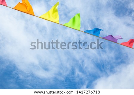The concept of a happy summer joy. Multicolored triangular flags develop against a blue sky with light clouds. Background image, minimalism, brightness. Copy space for text or logo.