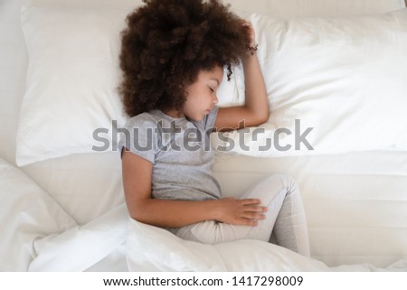 Adorable african american girl sleeping well in cozy bed, cute little kid lying on soft pillow napping alone, calm black child resting in good night healthy peaceful sleep in bedroom, top view above