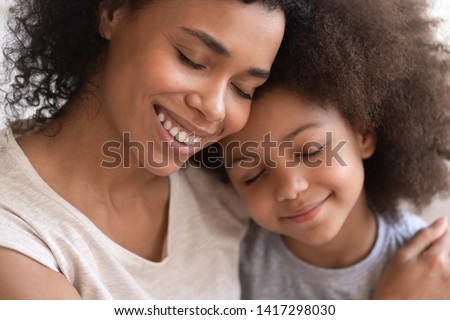 Loving affectionate family young african american mother holding embracing cute little kid daughter, happy black mom foster parent hug small mixed race child cuddling and bonding with eyes closed