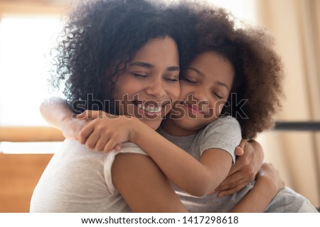 Cute affectionate african family foster parent mother and little kid daughter embrace cuddle feel connection, happy black mom hug small child girl enjoy tender warm moment of love with eyes closed