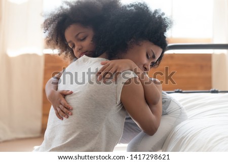 Cute small african american daughter hugging upset mother sit on bed, loving black mom embracing little child girl give support comforting helping in problem expressing empathy and unconditional love