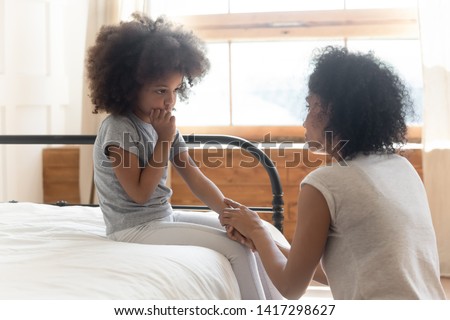Caring worried african american mother holding hand of sad little mixed race daughter talking giving support and comfort, black mom foster parent consoling small kid being bullied sit on bed at home Royalty-Free Stock Photo #1417298627