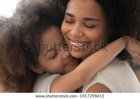Happy affectionate african family mom and cute little child daughter embrace with eyes closed, smiling foster parent mother and small kid girl hugging cuddling enjoy tender warm moment, close up view