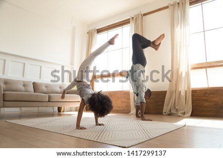 Sporty active african american family father and kid daughter doing handstand at home, healthy parent black dad with cute little child girl enjoy leisure gymnastic activity playing together at home