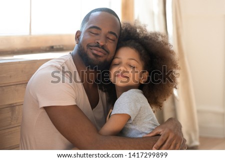 Loving african american family cute funny child daughter embrace black father feel love affection together, happy dad and little kid girl hug cuddling bonding with eyes closed at home on fathers day