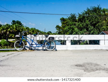 A blue bicycle built for two rests on a small white bridge railing waiting to be used on this clear blue summer day. Royalty-Free Stock Photo #1417321400