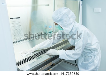A scientist in sterile coverall gown using alcohol 70% and cleanroom wipes for cleaning Biological safety cabinet(BSC.) in laboratory, before and after using bsc. ,decontamination,Cleanroom facility. Royalty-Free Stock Photo #1417332650