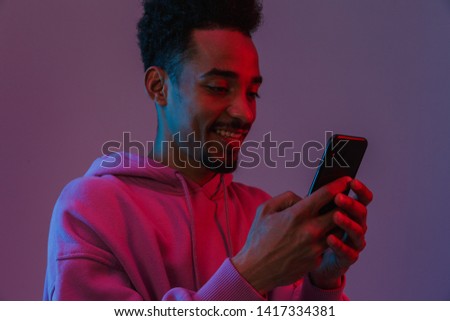 Portrait of young african american man in colorful hoodie making video call on cellphone isolated over violet background