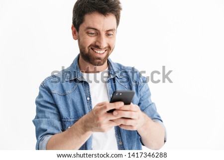 Portrait of a handsome bearded man wearing casual clothes standing isolated over white background, using mobile phone