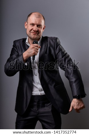 Happy emotional dancing and singing bald man listening the music in wireless headphone on dark grey background. Closeup portrait