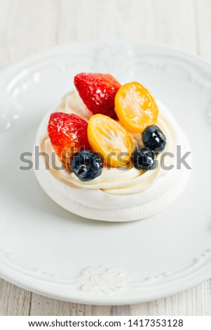 Pavlova's meringue cake with cream and glazed fruit on white plate on wooden table