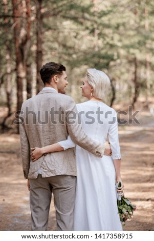 back view of just married couple embracing and looking at each other in forest