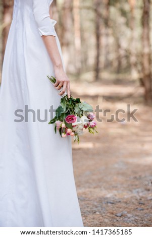 cropped view of bride in white attire holding wedding bouquet in forest