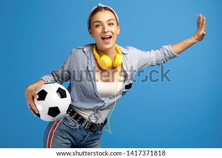 Photo of adorable young woman with yellow penny or skateboard, soccer ball and headphones dance over blue background.