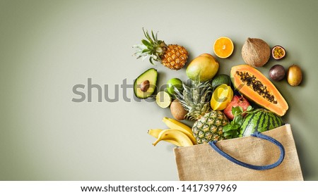 Panorama of fresh juicy tropical fruit overflowing from a reusable shopping bag onto a green background with copy space conceptual of a heathy vegetarian diet and nutrition Royalty-Free Stock Photo #1417397969