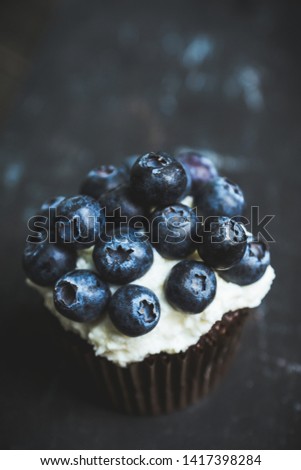 Homemade muffin with blueberry and cream cheese frosting on the rustic background. Selective focus.