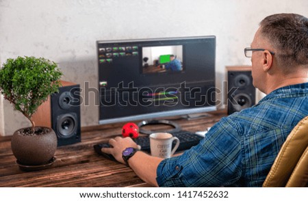 Businessman or photographer editing photographs on a large desk top monitor in an office in an over the shoulder view onto his desk