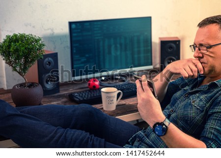 Businessman concentrating on reading his mobile phone as he relaxes in his chair with his feet up on the desk in his office