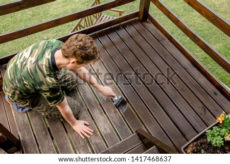 Top view of young man staining garden terrace wooden boards outdoors in spring. Terrace wood stain concept. Royalty-Free Stock Photo #1417468637
